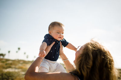 Grandmother holding grandson high while standing on beach