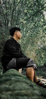 Side view of young man sitting in forest