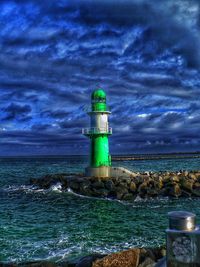 Lighthouse on beach against cloudy sky