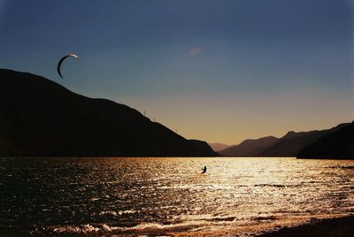 Silhouette person by sea against sky during sunset