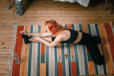 Positive athletic woman with red hair and tight sportswear stretching at home. 