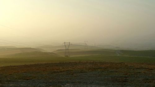 Electricity pylon on field against sky during foggy weather