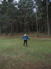 Boy in  blue jacket stands with his arms outstretched to the sides in clearing in middle of forest