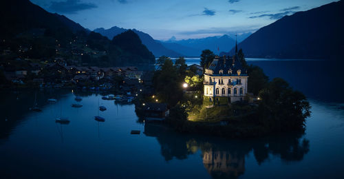 Illuminated buildings by lake against sky at dusk