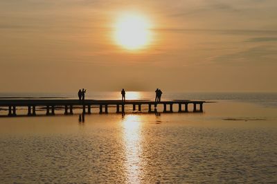 Silhouette people standing on pier over sea against sky during sunset