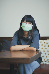 Smiling girl wearing mask sitting on sofa at home