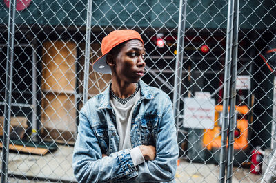 Portrait of young woman looking away against chainlink fence