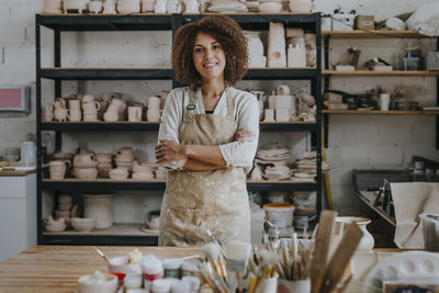 Smiling young potter standing with arms crossed at workshop