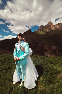 A young man and his wife stand in an embrace high in the mountains against the backdrop of epic