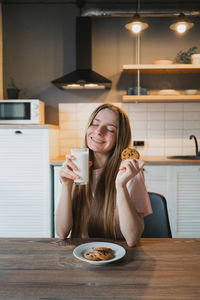 Portrait of smiling young woman drinking glass on table