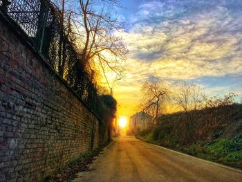 Road amidst bare trees against sky during sunset