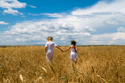 Rear view of mother and daughter walking on field against sky