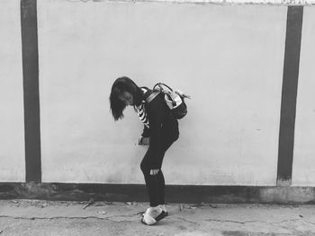 Side view of woman standing on footpath against wall