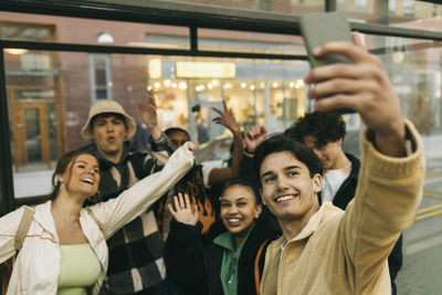 Happy man taking selfie with cheerful friends through smart phone at train station