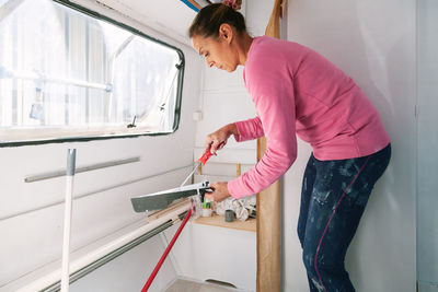 Side view of woman painting with paint roller at home