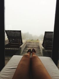 Low section of woman against lounge chairs in log cabin during foggy weather