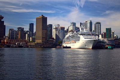 View of city at waterfront against cloudy sky