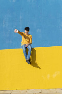 Full length of boy using phone while sitting against wall