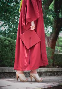 Low section of woman wearing graduation gown holding mortarboard