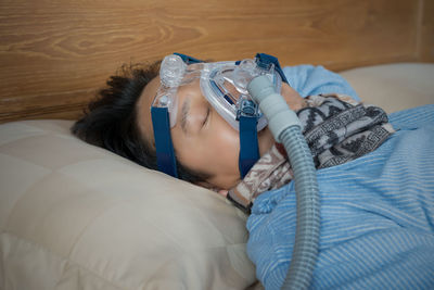 Mature man wearing oxygen mask while sleeping on bed