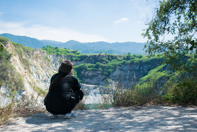 Man sitting on mountain against sky