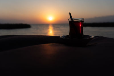 Drink on table by sea against sky during sunset