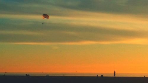 Silhouette people by beach against sky during sunset