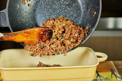 Chef pours pan-fried minced meat with onions and carrots into ceramic baking dish