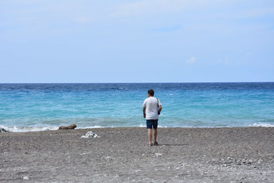 Rear view of man standing on beach against sky