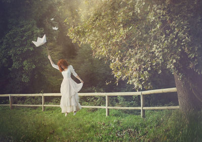 Woman with paper boat levitating over field