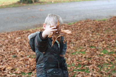 Boy throwing dry leaves while standing in autumn