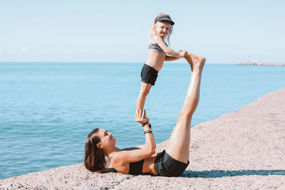 Mother and daughter exercising at beach against sky