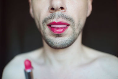 Midsection of transgender man with red lipstick against black background