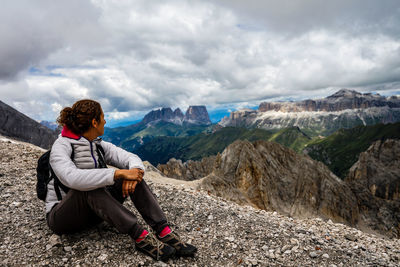 Man sitting on rock looking at mountains against sky