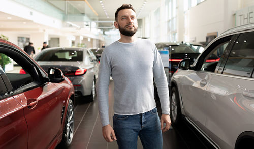 Portrait of man standing near car in showroom