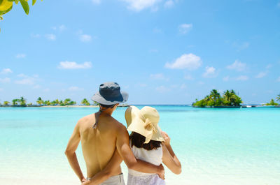 Rear view of couple standing at beach against sky during summer