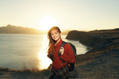 Smiling young woman standing on land against sky during sunset