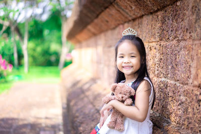 Portrait of cute girl holding toy standing by wall outdoors