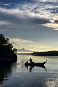 Silhouette people sitting on river against sky during sunset