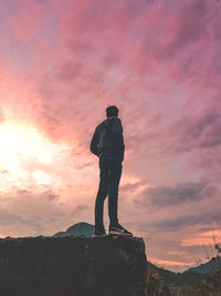 Rear view of man standing on rock against sky during sunset