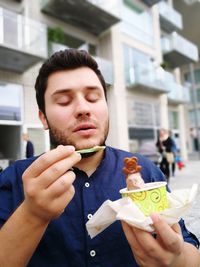 Man holding cup of ice cream sitting against building 