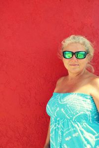 Portrait of woman wearing sunglasses standing against red wall