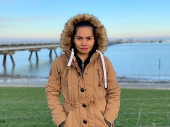 Portrait of young woman standing in park against sky during winter