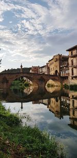 Arch bridge over river by buildings against sky