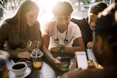 Teenage girls and boys surfing internet on mobile phones while sitting in cafe