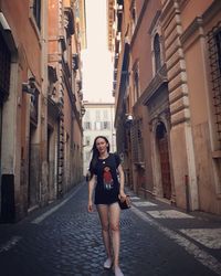 Portrait of young woman standing on alley amidst buildings in city