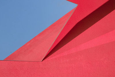 Low angle view of red wall with skylight against clear blue sky