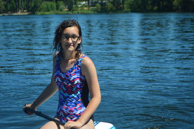 Portrait of smiling woman sitting on paddleboard at lake