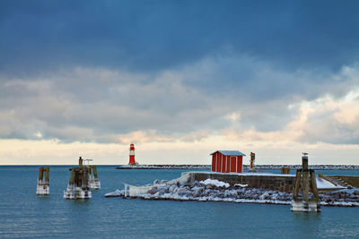 Mid distance of lighthouse on groyne at sea against cloudy sky in winter