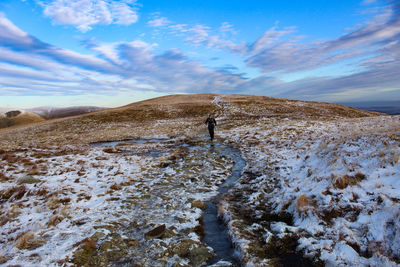 Man walking over stream amidst snow covered landscape